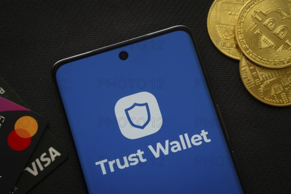 Dhaka, Bangladesh- 30 Sep 2025: Smartphone displaying Trust Wallet logo surrounded by Bitcoin coins and payment cards