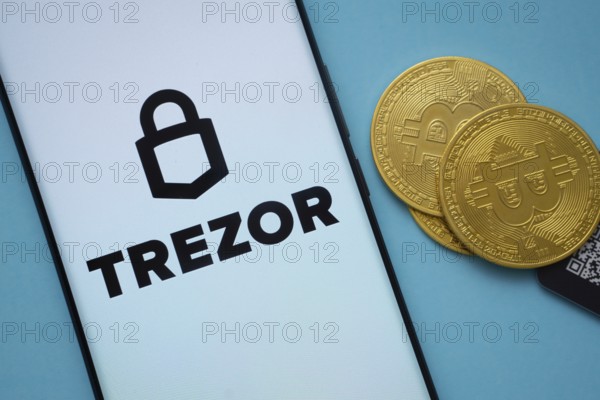 Dhaka, Bangladesh- 30 Sep 2025: Trezor logo on smartphone screen near Bitcoin coin and QR code on blue background