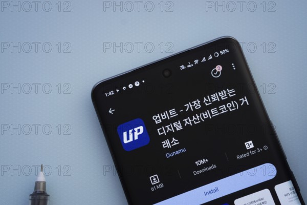 Dhaka, Bangladesh- 29 May 2025: On a blue surface, a smartphone displays the Upbit app within the Google Play Store