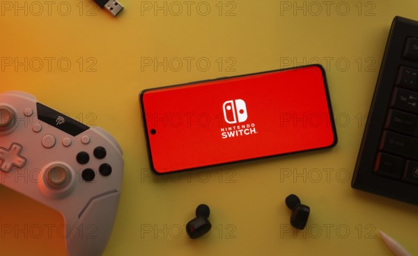Dhaka, Bangladesh- 15 July 2025: Smartphone with nintendo switch logo, game controller, and earbuds on a yellow background