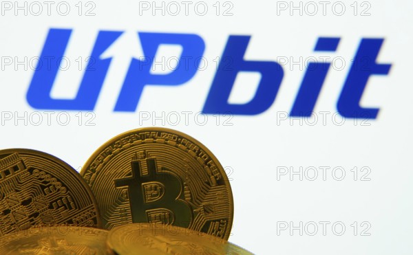 Dhaka, Bangladesh- 18 Sep 2025: Close-up of Bitcoin coins with thex Upbit logo visible on a screen in the background