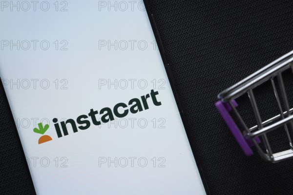 Dhaka, Bangladesh- 03 July 2025: A smartphone displaying the Instacart logo next to a miniature shopping cart on a background