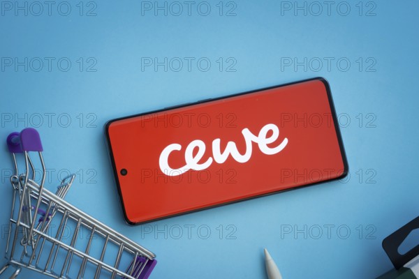 Dhaka, Bangladesh- 03 July 2025: Smartphone displaying Cewe logo with shopping cart on a blue background