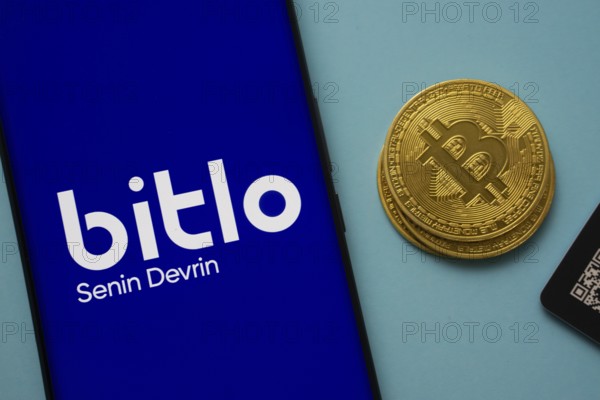 Dhaka, Bangladesh- 03 Sep 2025: Bitlo.com logo on smartphone screen near Bitcoin coin and QR code on blue background