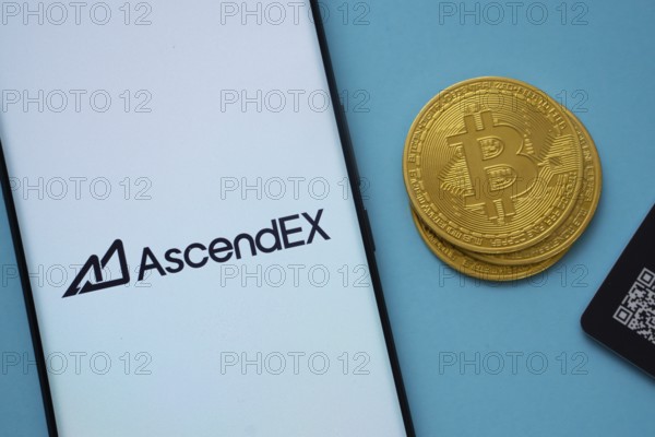 Dhaka, Bangladesh- 02 June 2025: AscendEX logo on smartphone screen near Bitcoin coin and QR code on blue background