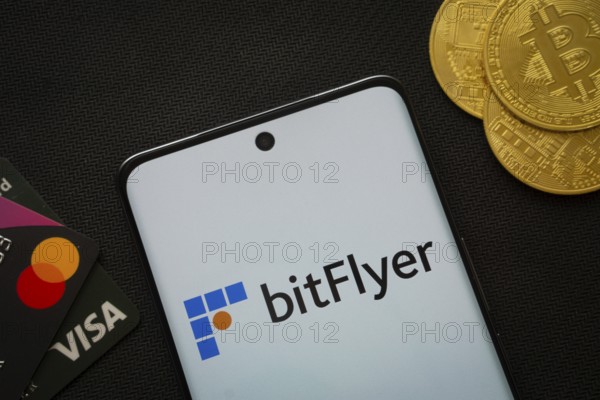 Dhaka, Bangladesh- 02 June 2025: Smartphone displaying Bitflyer logo surrounded by Bitcoin coins and payment cards