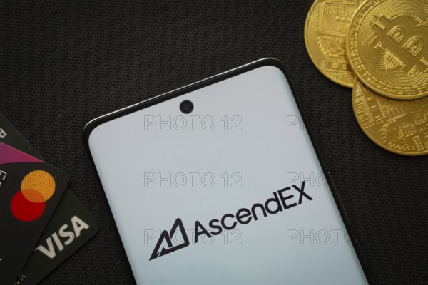 Dhaka, Bangladesh- 02 June 2025: Smartphone displaying AscendEX logo surrounded by Bitcoin coins and payment cards