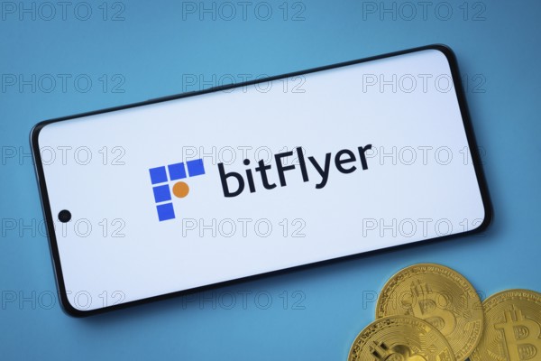 Dhaka, Bangladesh- 02 June 2025: Bitflyer logo on smartphone screen near Bitcoin coin and QR code on blue background