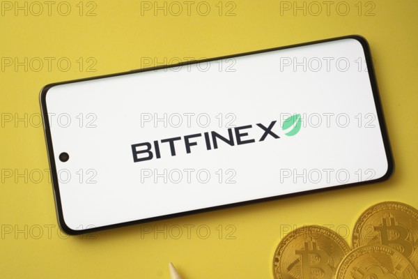 Dhaka, Bangladesh- 15 June 2025: Bitfinex logo on smartphone screen near Bitcoin coin and QR code on background