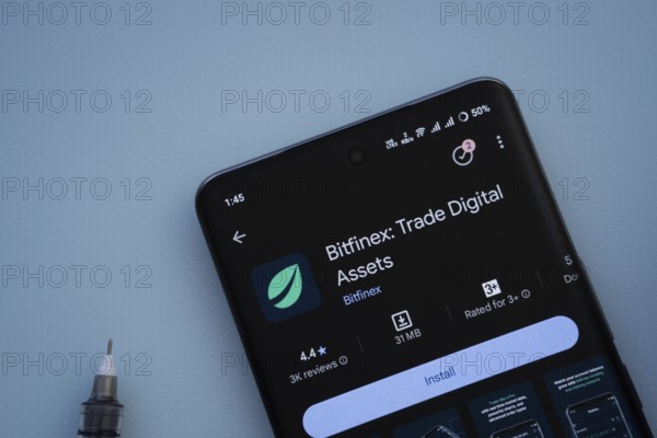 Dhaka, Bangladesh- 29 May 2025: On a blue surface, a smartphone displays the Bitfinex app within the Google Play Store