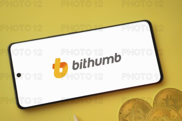 Dhaka, Bangladesh- 07 May 2025: Bithumb logo on smartphone screen near Bitcoin coin and QR code on background