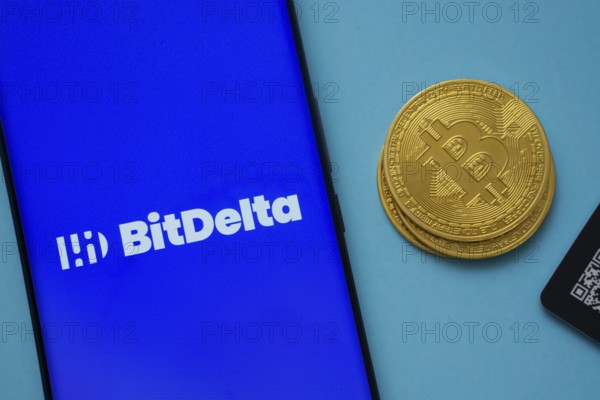 Dhaka, Bangladesh- 07 May 2025: BitDelta logo on smartphone screen near Bitcoin coin and QR code on blue background