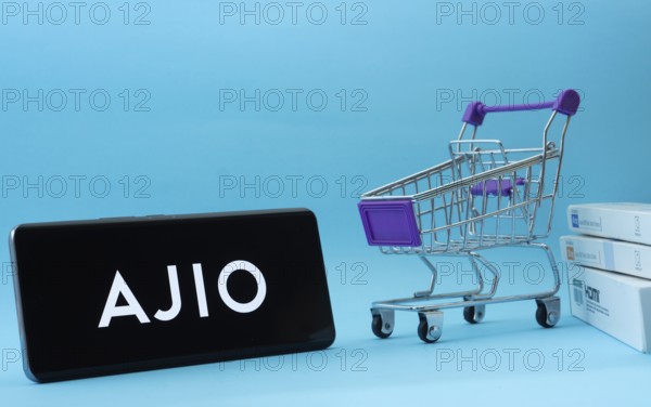 Dhaka, Bangladesh- 03 July 2025: Smartphone with AJIO logo next to a small shopping cart and boxes against a blue background