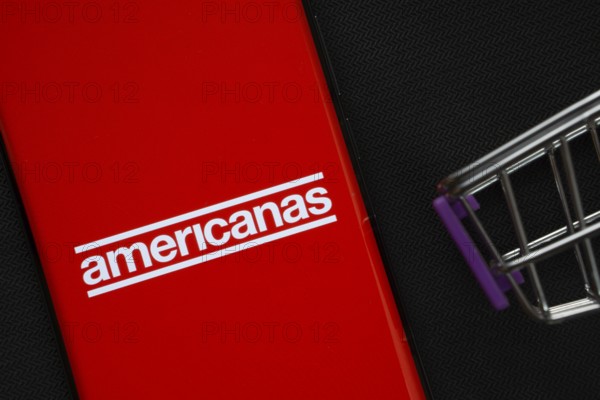 Dhaka, Bangladesh- 03 July 2025: A smartphone displaying the Americanas logo next to a miniature shopping cart on a background