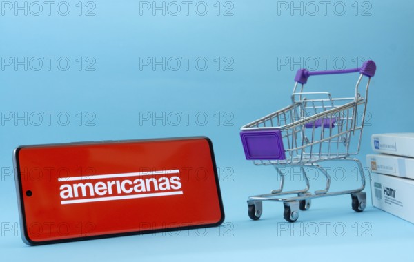 Dhaka, Bangladesh- 03 July 2025: Smartphone with Americanas logo next to a small shopping cart and boxes against a blue background