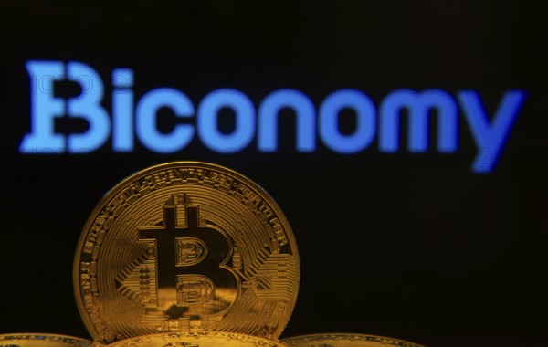 Dhaka, Bangladesh- 02 June 2025: Close-up of Bitcoin coins with the Biconomy logo visible on a screen in the background