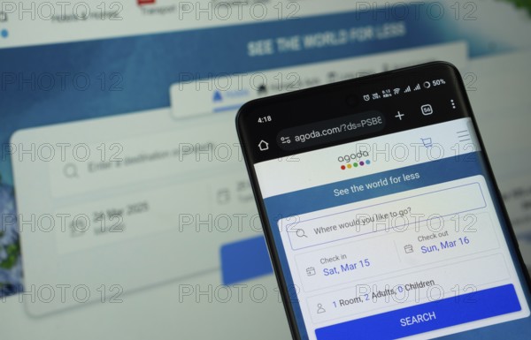 Dhaka, Bangladesh - 27 July 2025: The logo of Agoda is displayed on a smartphone screen, and the website is visible on a computer screen in the background