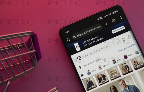 Dhaka, Bangladesh- 23 June 2025: A smartphone displaying the AJIO website with a shopping cart is shown on a vibrant background