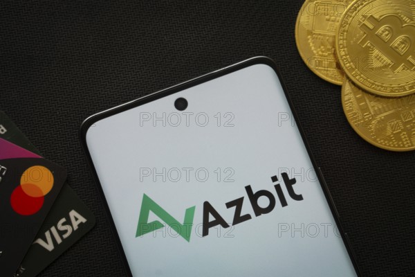 Dhaka, Bangladesh- 02 June 2025: Smartphone displaying Azbit logo surrounded by Bitcoin coins and payment cards