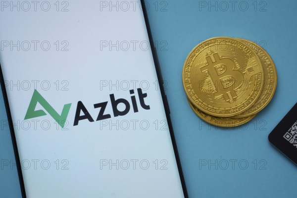 Dhaka, Bangladesh- 02 June 2025: Azbit logo on smartphone screen near Bitcoin coin and QR code on blue background