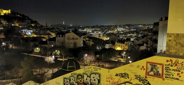 Nighttime city scene with glowing lights and graffiti along a wall, view of the city, Lisbon, Portugal