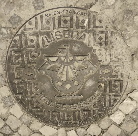 Engraved manhole cover on cobblestones with decorative patterns and a city coat of arms, Lisbon, Portugal