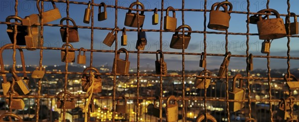 Metal grid full of love locks against an illuminated city backdrop in the evening, view of Lisbon in the background, Lisbon, Portugal