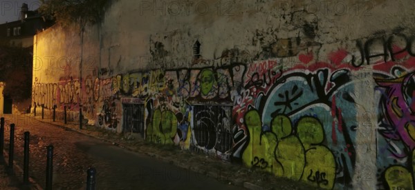 Graffiti-covered wall in a nighttime street scene with atmospheric street light, Lisbon, Portugal