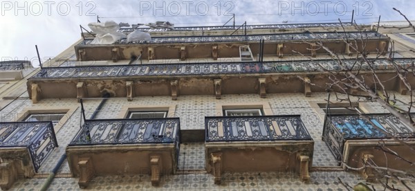 Old building with decorated balconies from which laundry hangs and tile façade under a blue sky, Lisbon, Portugal