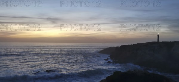A lighthouse on the edge of the coast at sunset with waves in the sea, sunset over a peaceful ocean with rocks in the foreground, hiking the fisherman's trail, rota vicentina, Porto Covo, Alentejo region, Portugal