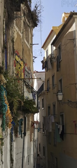 A narrow alley between old buildings with graffiti and hung laundry, Lisbon, Portugal