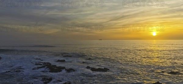 Colourful sunset over the calm sea with a ship on the horizon, hiking the Fisherman's Trail, Rota Vicentina, Porto Covo, Alentejo region, Portugal