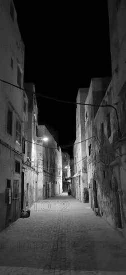 Black and white shot of a dark alley in Essaouira with sparse lighting and historic buildings, Essaouira, Morocco