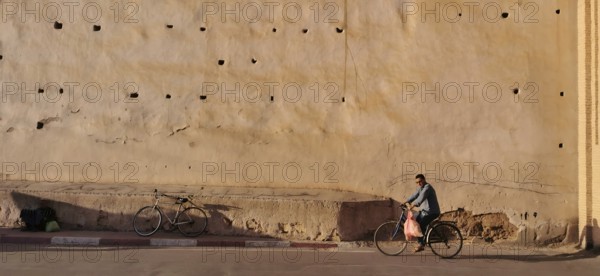 An old city wall with a cyclist riding along in the shade, Taroudannt, Morocco