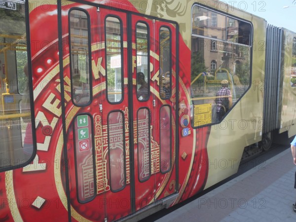 A tram with Pilsner Urquell painting stops at a sunny city stop, Pilsen, Czech Republic