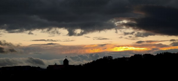 A dramatic sunset with dark clouds over a hilly landscape