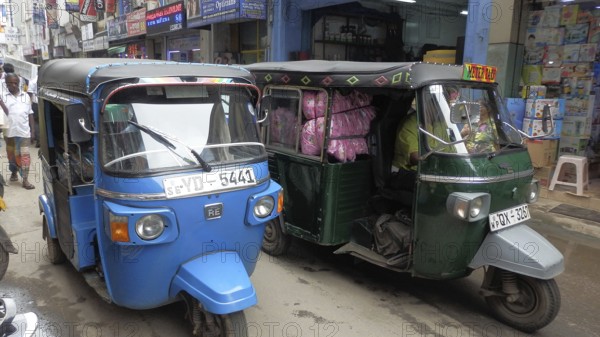 Colourful tuktuks park along a lively city street with shops, Sri Lanka