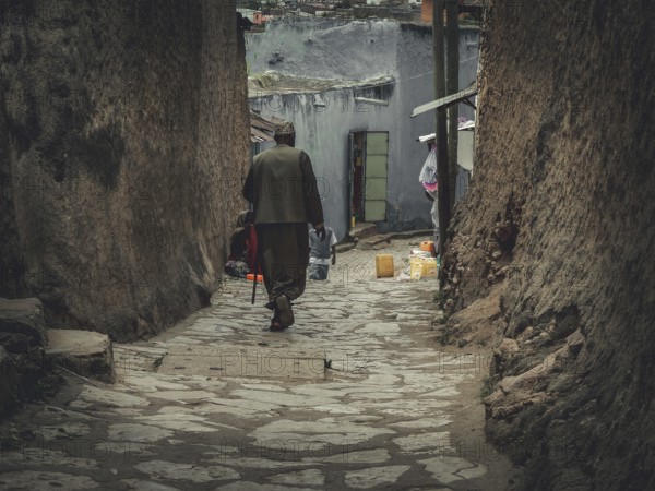 Man in a long coat walks through a narrow, stone-paved alley in Harar, Ethiopia