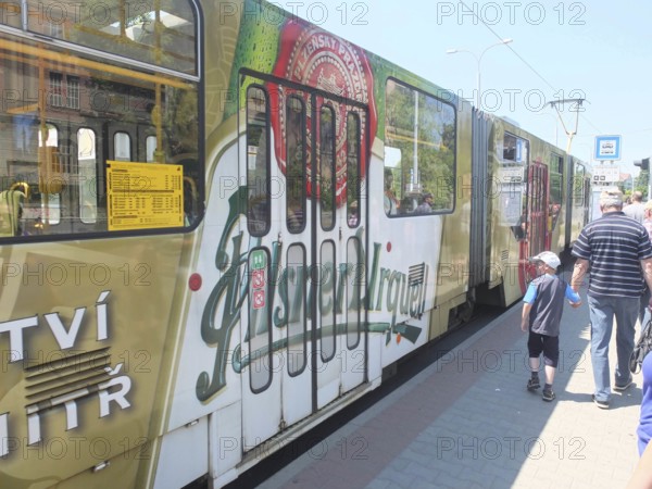 A tram with an advertising message from Pilsner Urquell passes a bus stop, Pilsen, Czech Republic