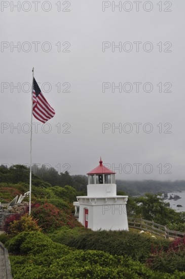 White lighthouse with red roof near the coast, American flag in the foreground, surrounded by greenery, Redwood National Park, California, USA