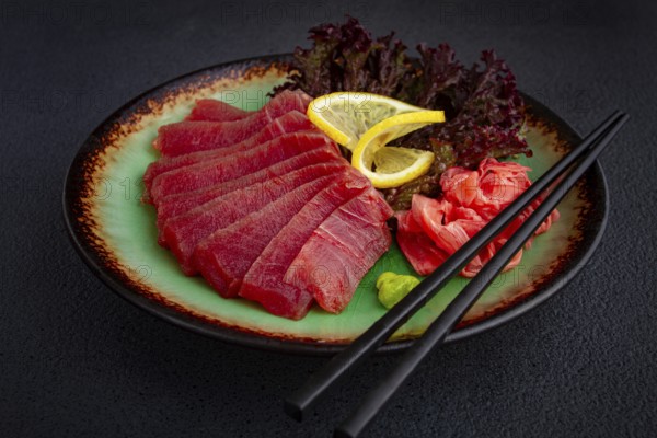 Fresh tuna sashimi served with lemon, wasabi, and pickled ginger on a dark background