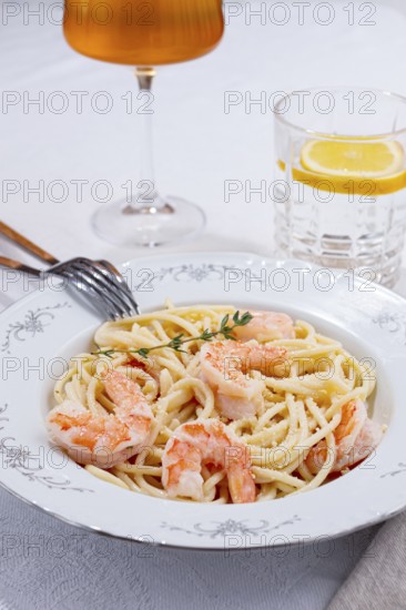 Pasta with shrimp and thyme, served on a white plate, with a glass of white wine, the table is set, Gourmet dinner, on a linen tablecloth, no people