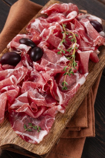 Freshly cut dried meat, served with olives and herbs, on a wooden chopping board, no people