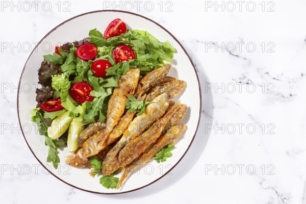 Fried crispy mullet fish, with fresh salad, on a plate with lime, no people