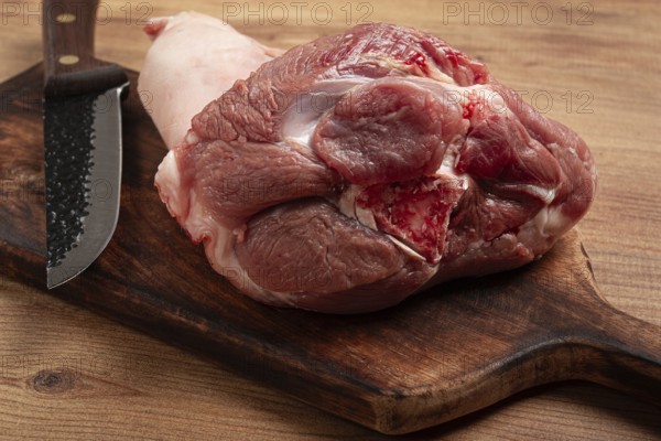 Raw pork knuckle, on a wooden chopping board, close-up, top view, no people