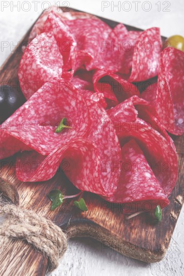 Sliced salami sausage, on a wooden chopping board, decorated with olives and herbs, close-up, no people