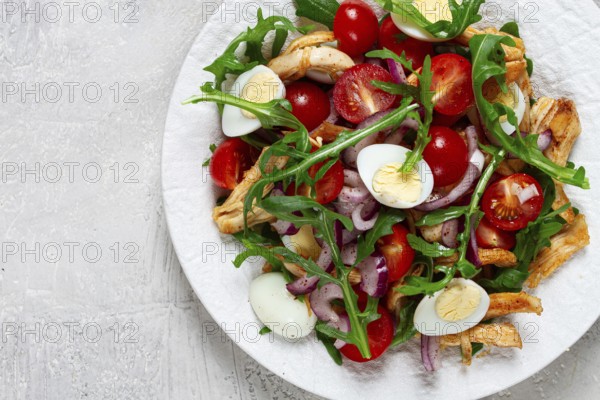 A warm salad with fried chicken fillet, arugula and cherry tomatoes, and boiled quail eggs, on a white plate, no people
