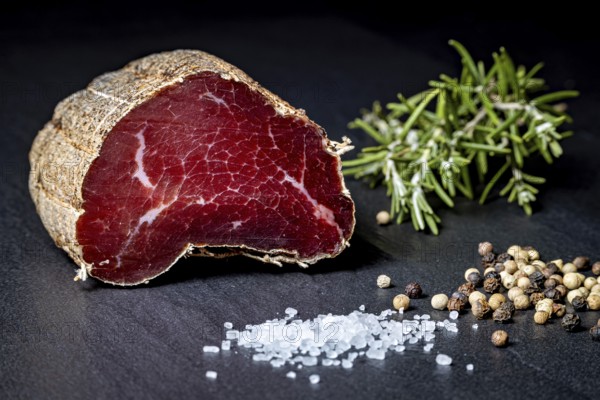 Delicate sausage piece on slate plate with salt and peppercorns, delicatess ham fresh from the butcher