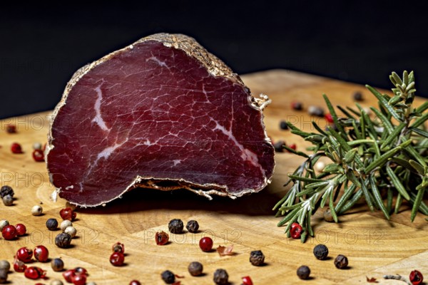 Delicious piece of raw sausage on wooden board decorated with peppercorns, delicacy ham fresh from the butcher