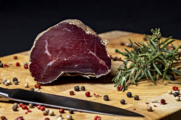 Delicatesswurst on wooden board decorated with peppercorns and rosemary, delicatess ham fresh from the butcher